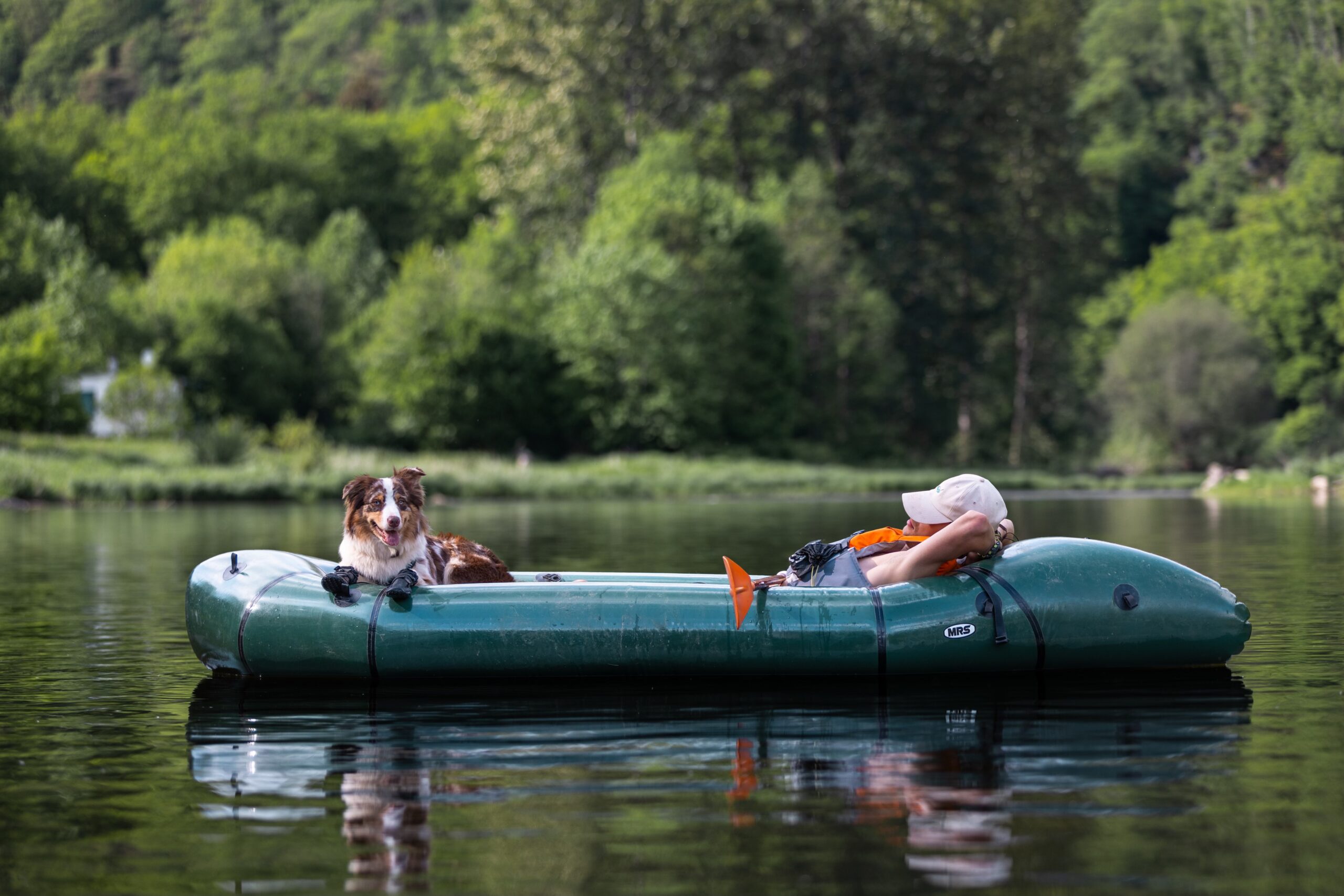 homme couché dans un packraft avec un chien